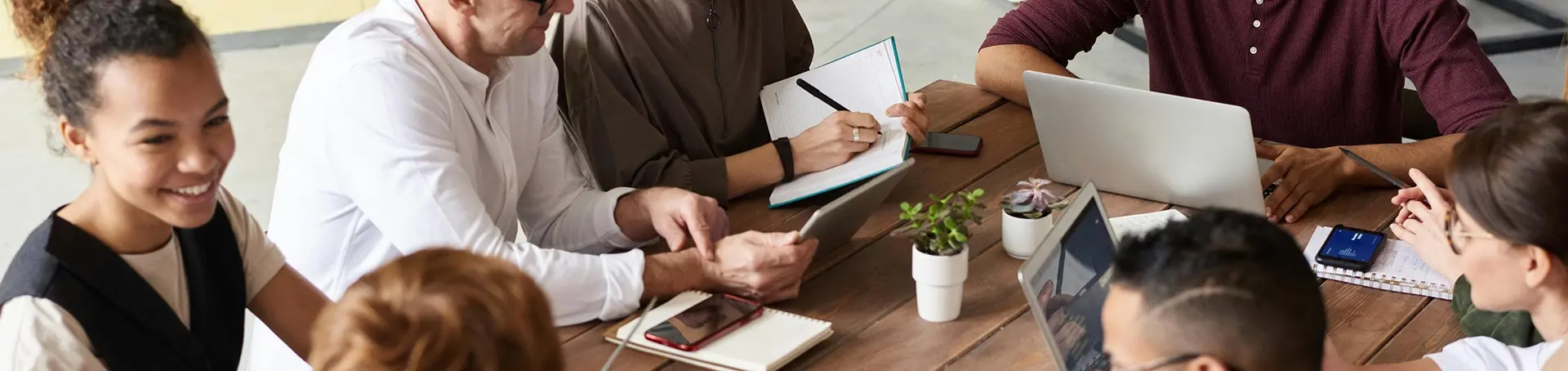 A marketing team having a discussion around a table, which has notebooks, pens and laptops on it