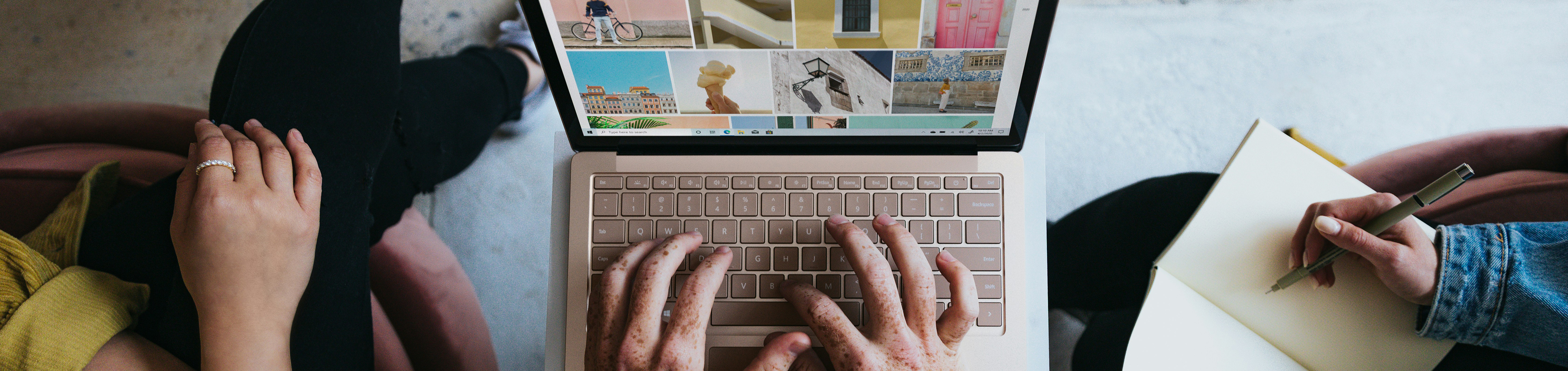 Aerial view of the hands of three people discussing a marketing plan with a laptop and notepad in view